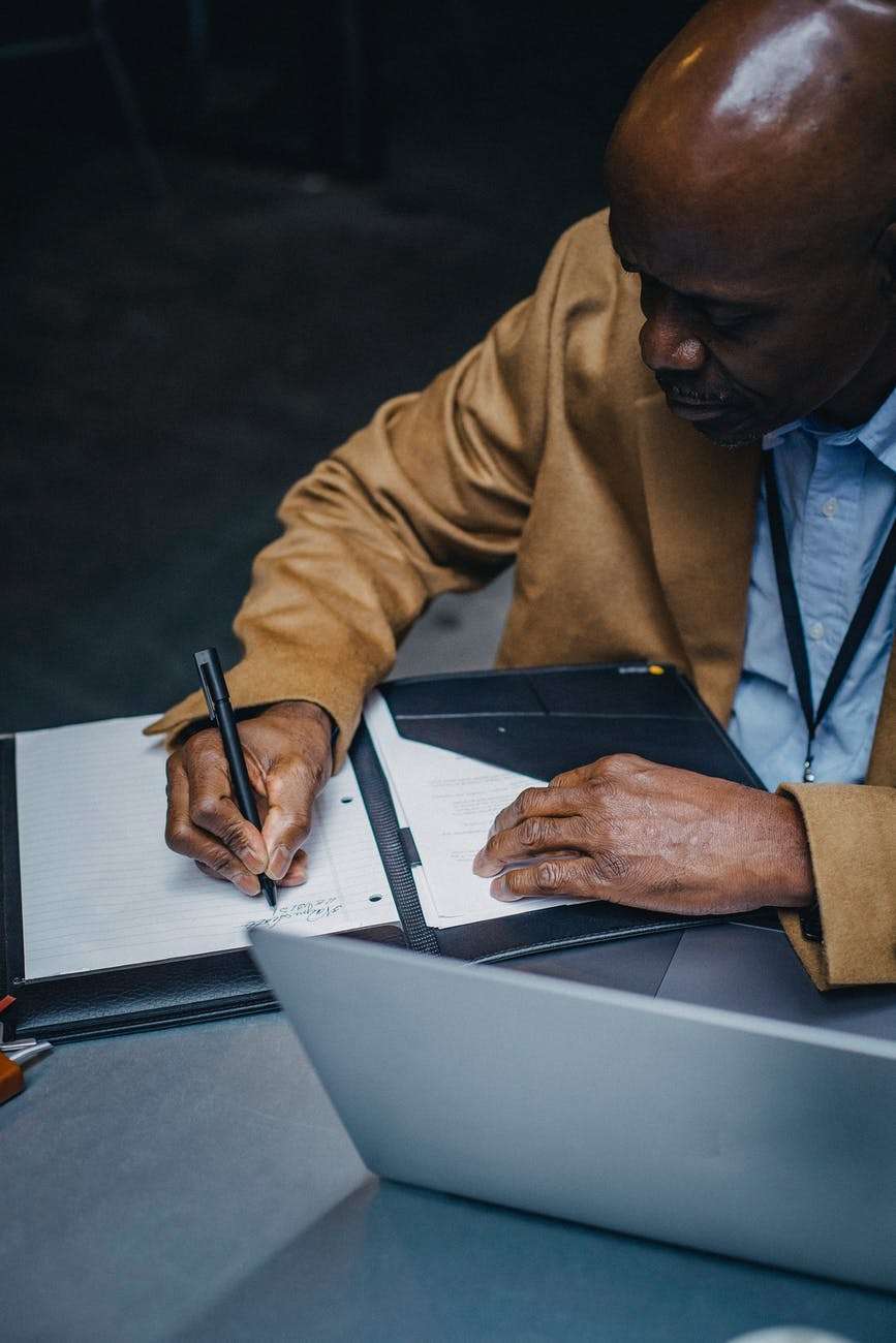 an image of a man writing on a booklet of foolscaps with a pen